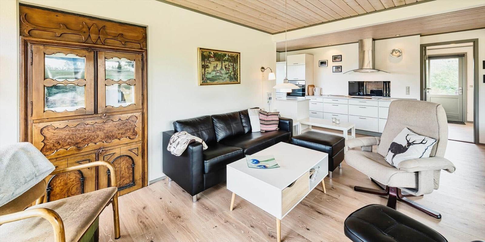 Wohnzimmer mit Sofa, Sessel und Küchenbereich im Hintergrund.
