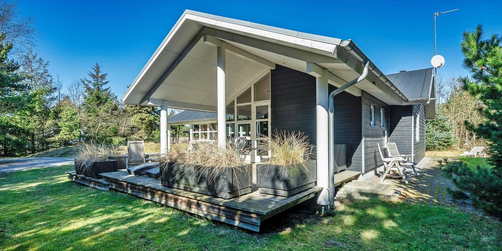 Moderne Holzhütte mit Terrasse, Sitzgelegenheiten und Blick auf Wald.