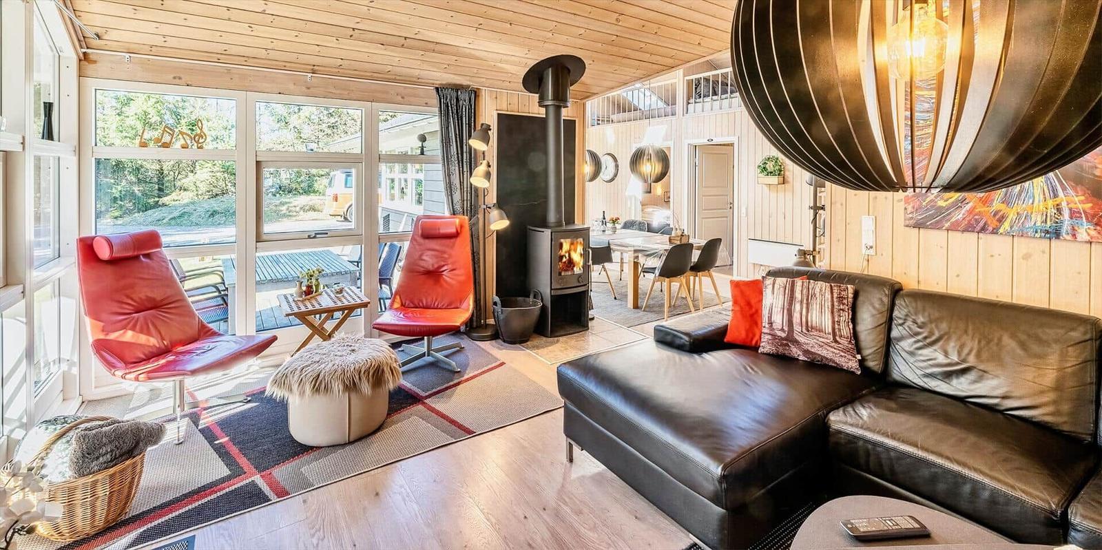 Wohnzimmer mit Sofa, roten Sesseln und Kamin. Holzwände und große Fenster.