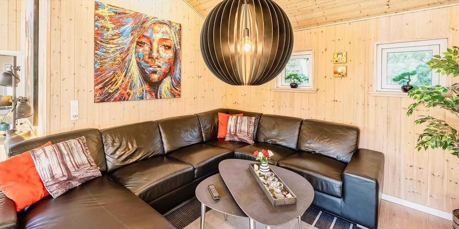 Schwarzes Ledersofa mit Kissen, runder Tisch und Wandbild in Holzwandung.