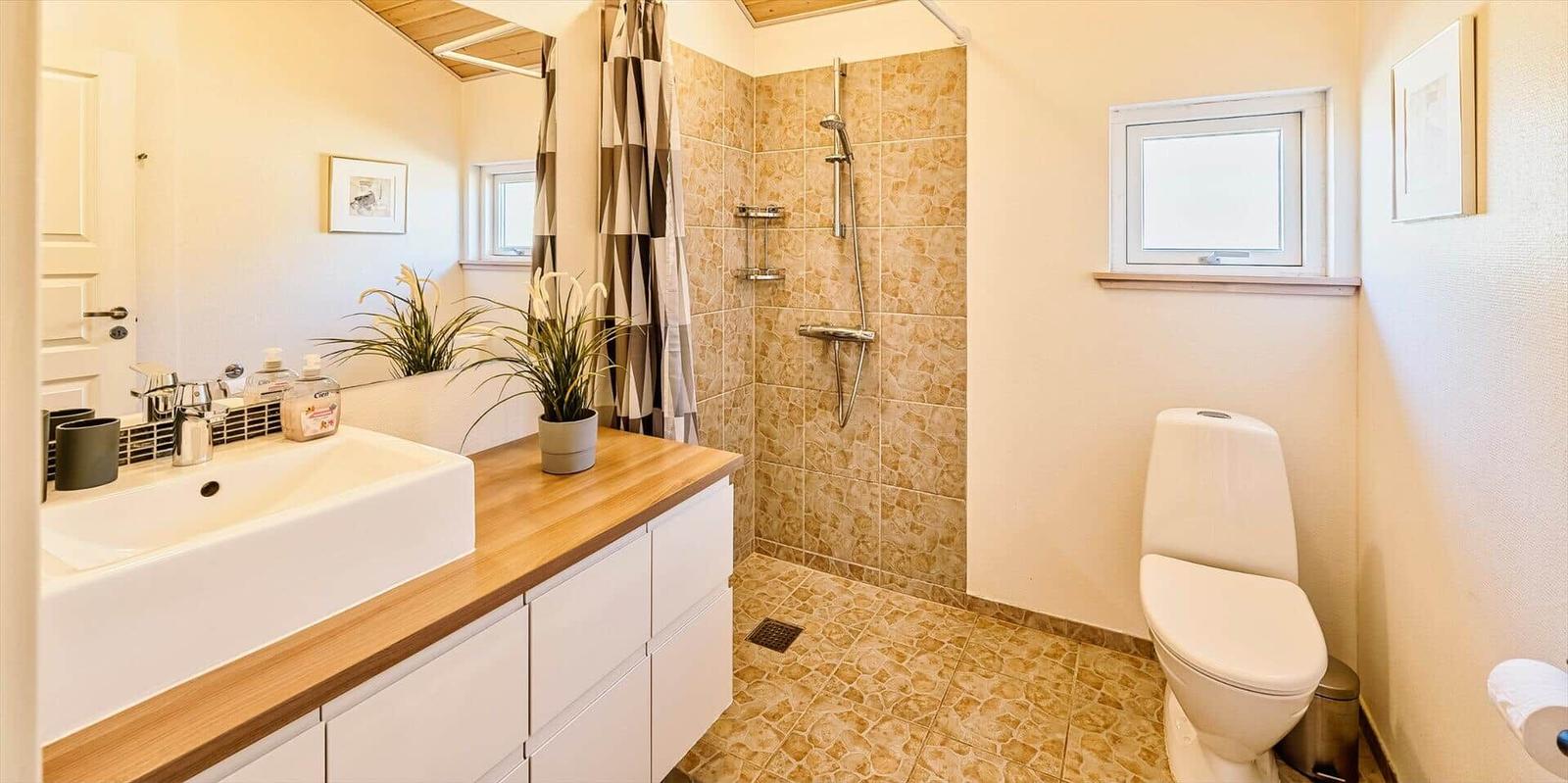 Badezimmer mit Dusche, Toilette und Waschtisch mit Holzplatte.