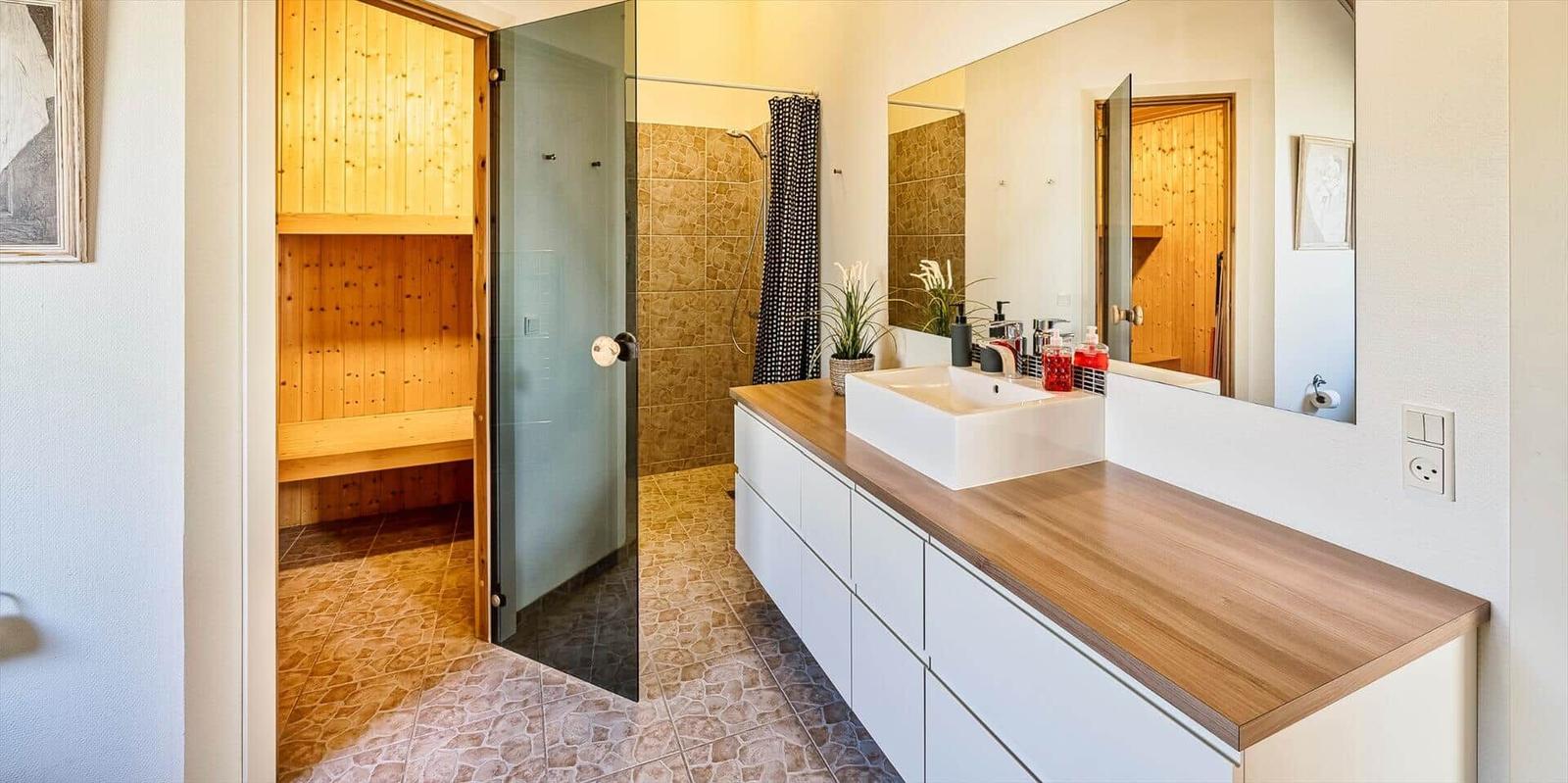 Badezimmer mit Dusche, Waschtisch und Holzsauna