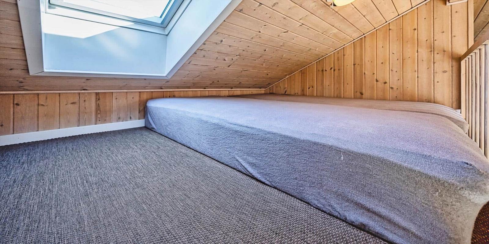 Schlafzimmer mit Dachschräge, Holzwänden und Dachfenster. Bett mit grauer Bettwäsche.