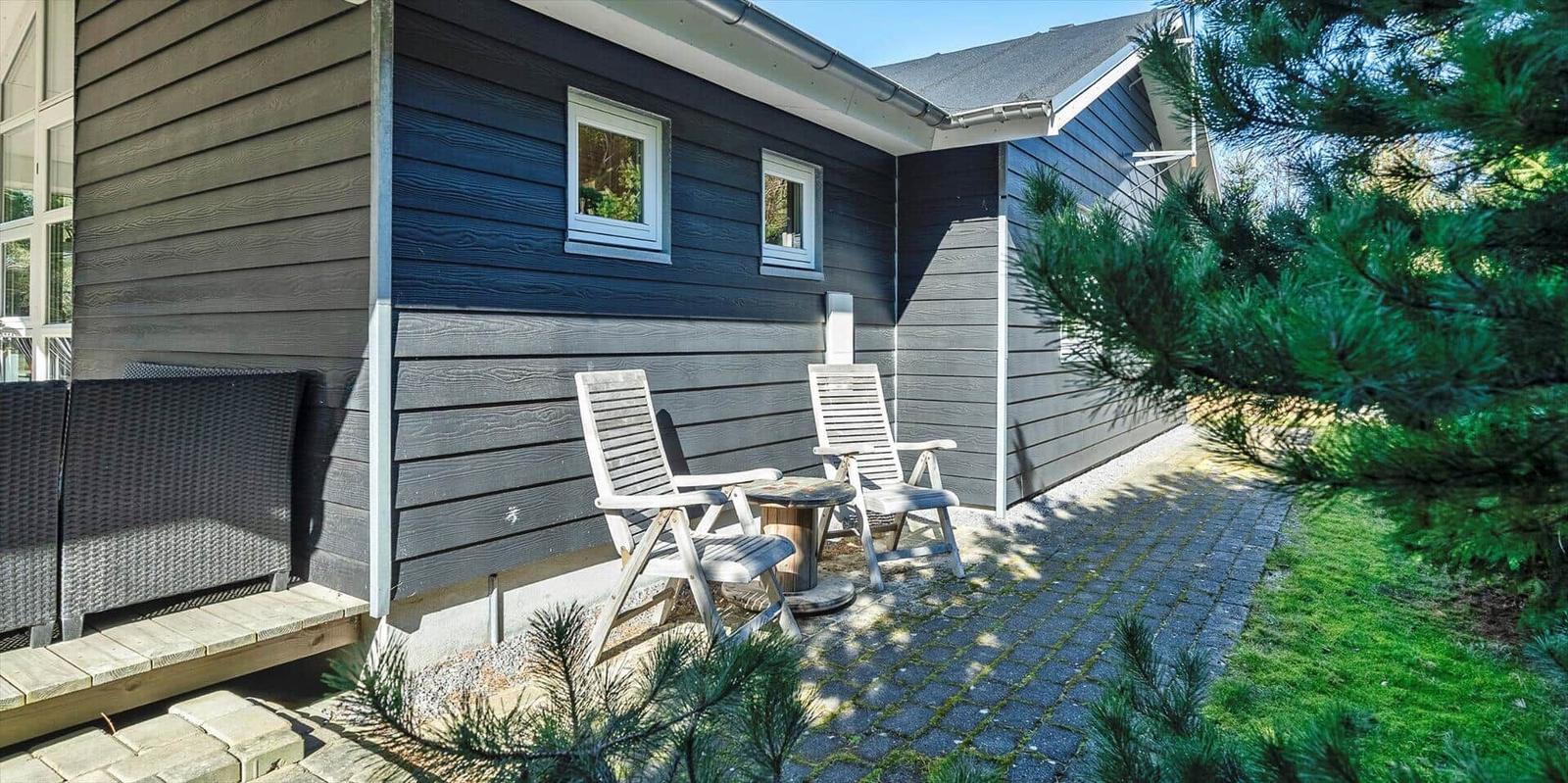 Außenbereich mit zwei Stühlen und Tisch vor einem Haus mit Holzfassade.