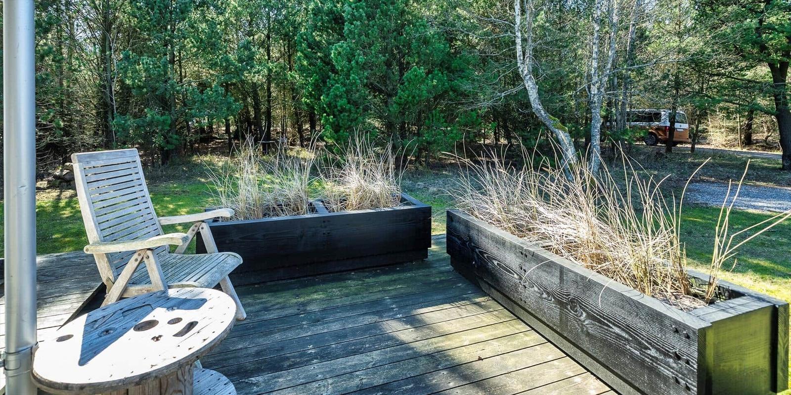 Terrasse mit Holzbank, Sitzgelegenheit und Pflanzenbeeten im Wald.