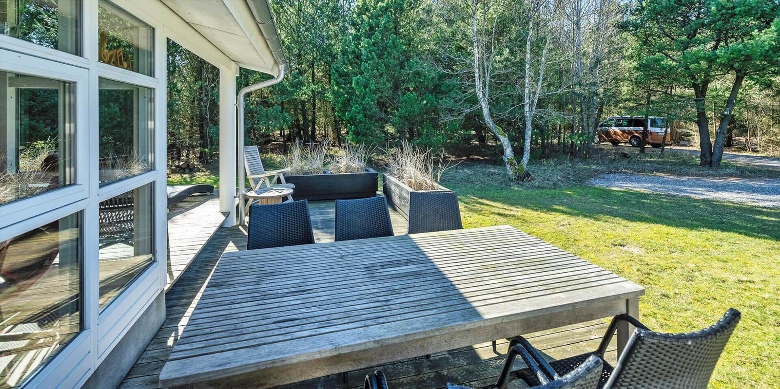 Terrasse mit Tisch und Stühlen, umgeben von Grün und Bäumen.