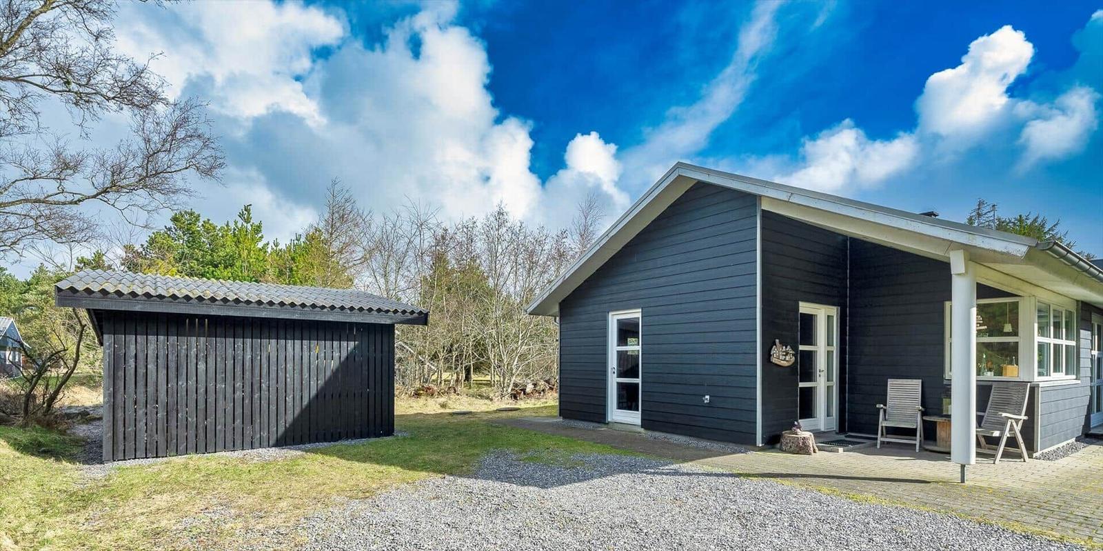Schwarzes Holzhaus mit Terrasse und Garten. Nebenhaus mit Schiebetür.