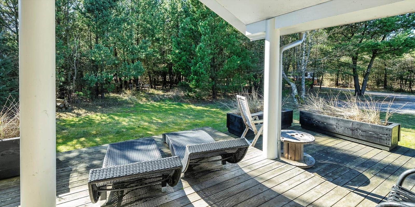 Terrasse mit Liegestühlen und Blick auf Wald und Grünfläche.