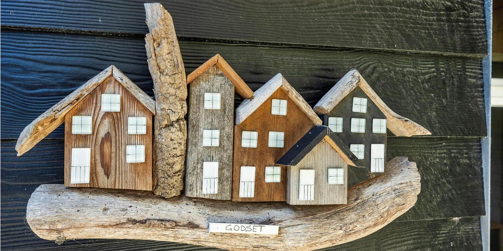 Holzfiguren von Häusern auf einem Ast, mit dem Schriftzug GODSET.