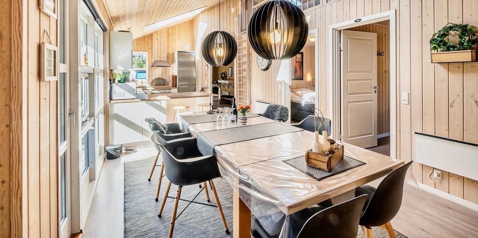 Essbereich mit Tisch und Stühlen, Küche im Hintergrund, Holzwände und moderne Beleuchtung.