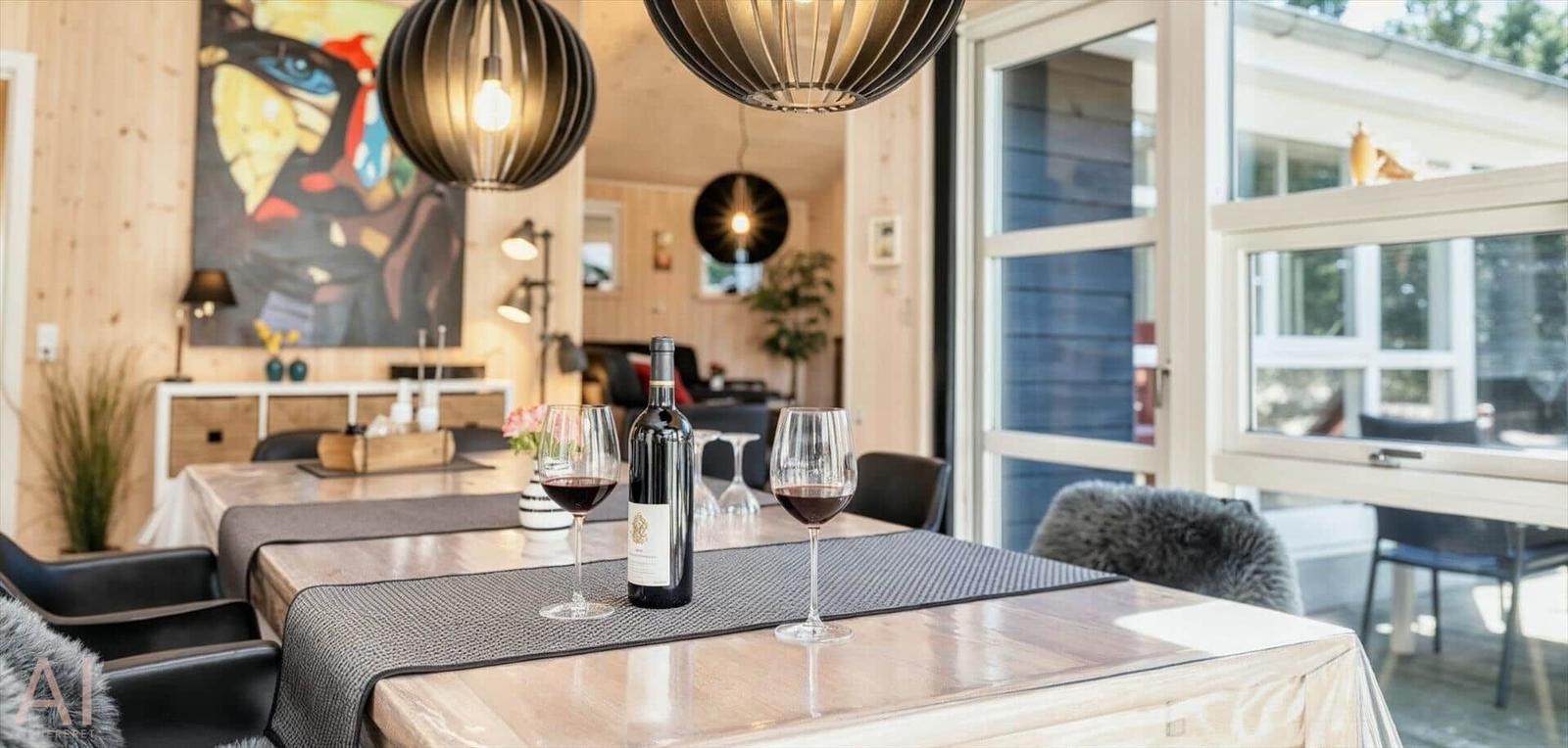 Esstisch mit Weinflasche und Gläsern vor großem Fenster und Holzwand