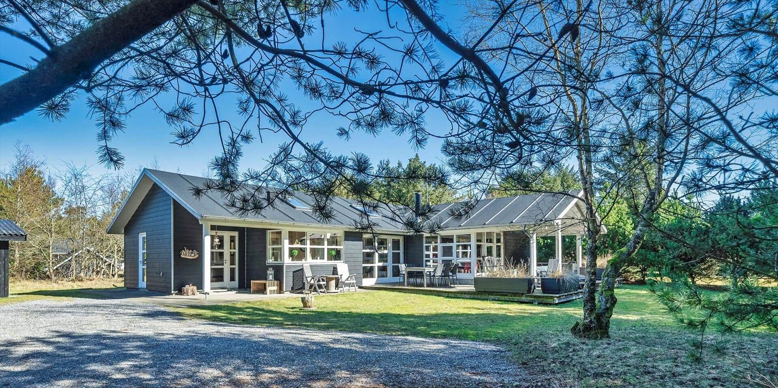 Ein modernes Haus mit Terrasse und Garten unter Bäumen.