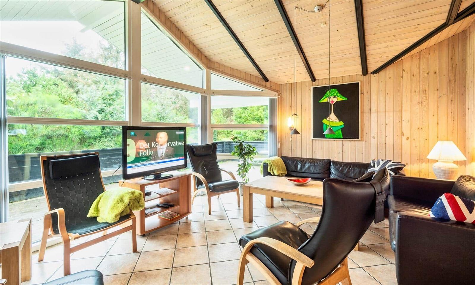 Wohnzimmer mit Holzwänden, großen Fenstern und schwarzen Ledermöbeln.