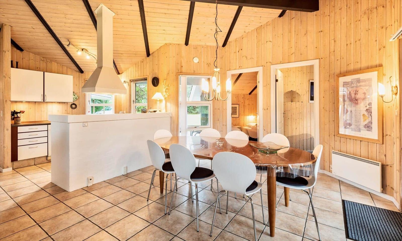 Küche und Essbereich mit Holzwand und Holzdach, weißer Küchenzeile und Esstisch mit Stühlen.