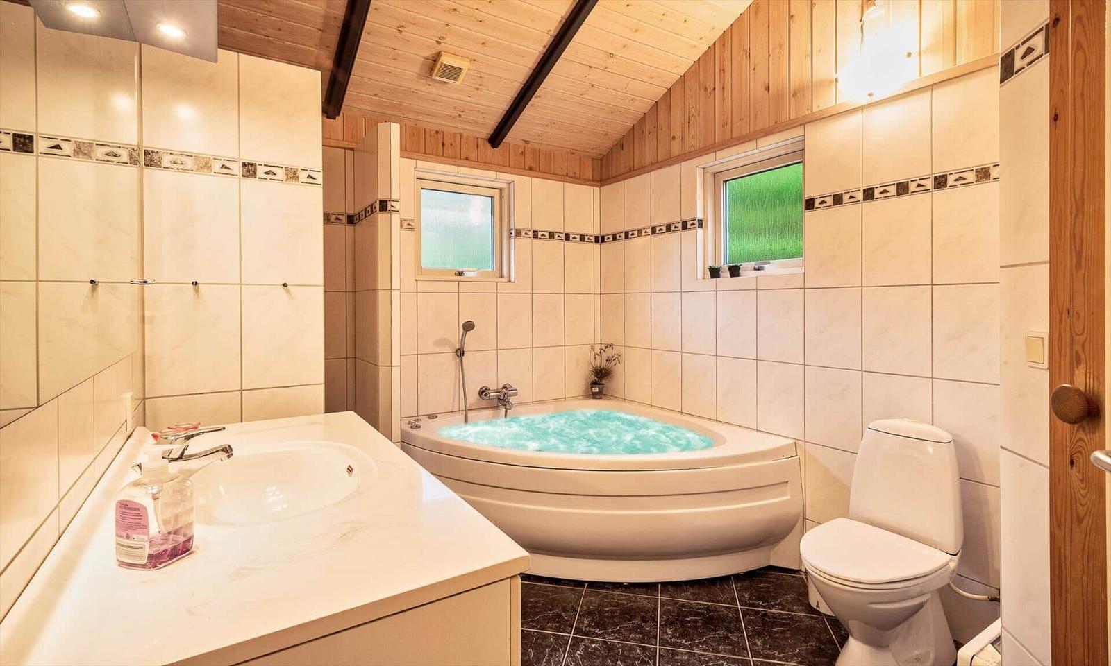 Bad mit Whirlpool, Waschbecken und Toilette. Holzdecke und Fenster mit grünem Glas.