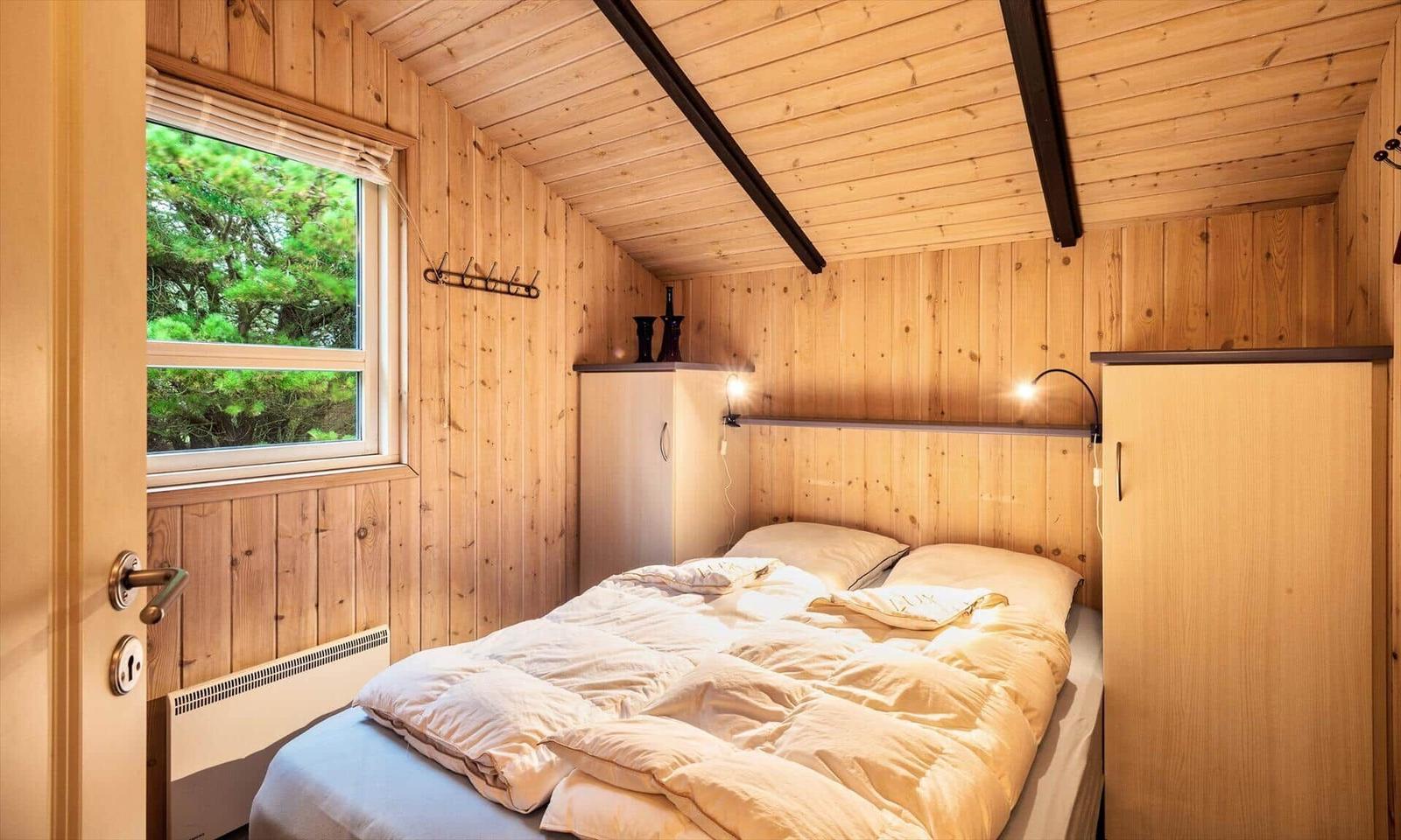 Schlafzimmer mit Holzwand, Bett, Fenster und Kleiderhaken.