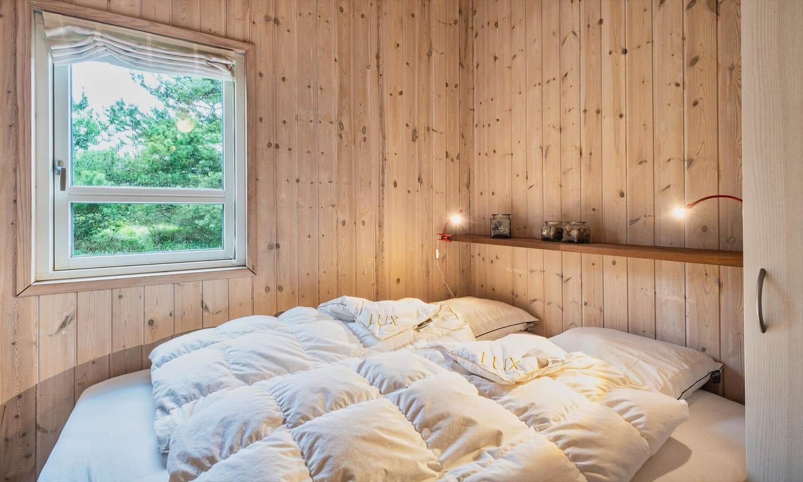 Schlafzimmer mit Holzwand, Fenster und Bett mit weißen Bettwäsche.