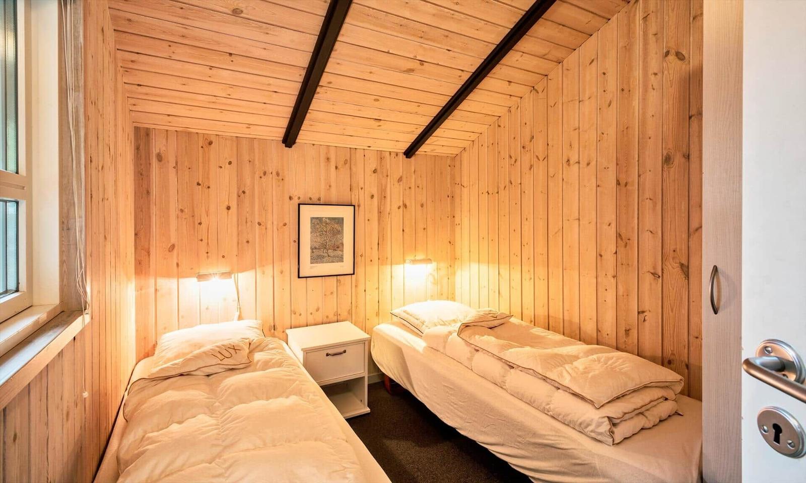 Zwei Betten in einem holzverkleideten Zimmer mit Fenster und Nachttisch.
