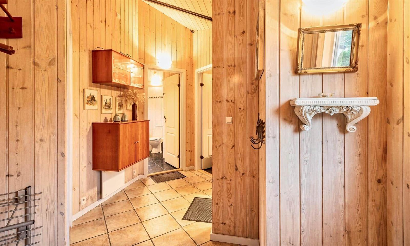 Flur mit Holzwand, Schrank, Spiegel und Bad im Hintergrund.