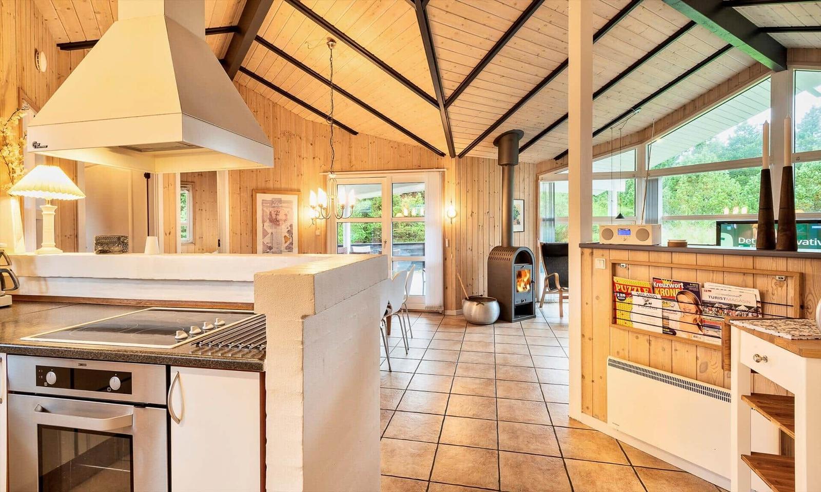 Küche mit Kochfeld und Backofen, Holzdecke, Holzwand und Kaminofen im Wohnbereich.