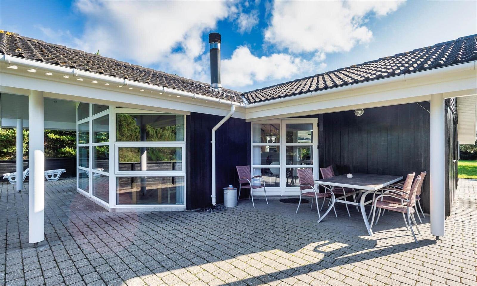 Terrasse mit Tisch, Stühlen und Glaswänden. Schwarze Fassade und Ziegeldach.