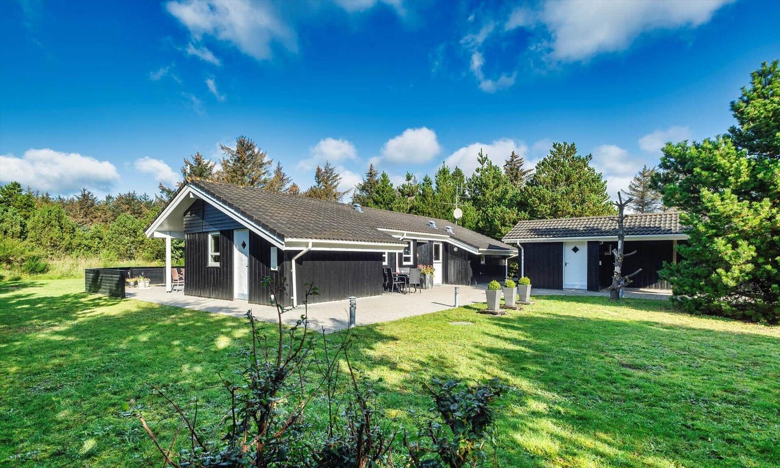Schwarze Holzhütte mit Terrasse und Garten unter blauem Himmel.