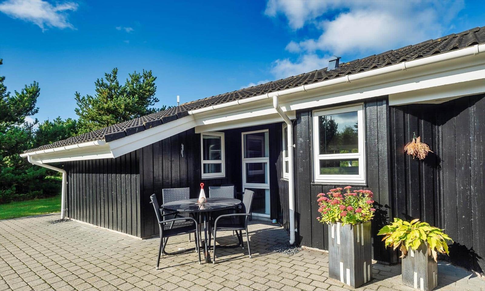 Schwarzes Holzhaus mit Terrasse, Tisch, Stühlen und Pflanzen.