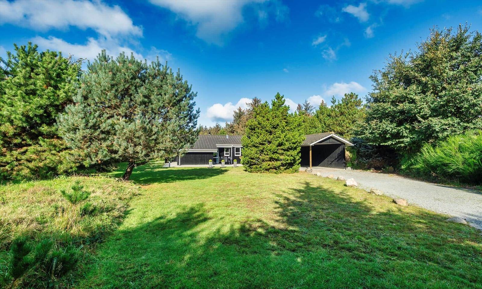 Schwarzes Haus mit Garage, umgeben von Gras und Bäumen unter blauem Himmel.