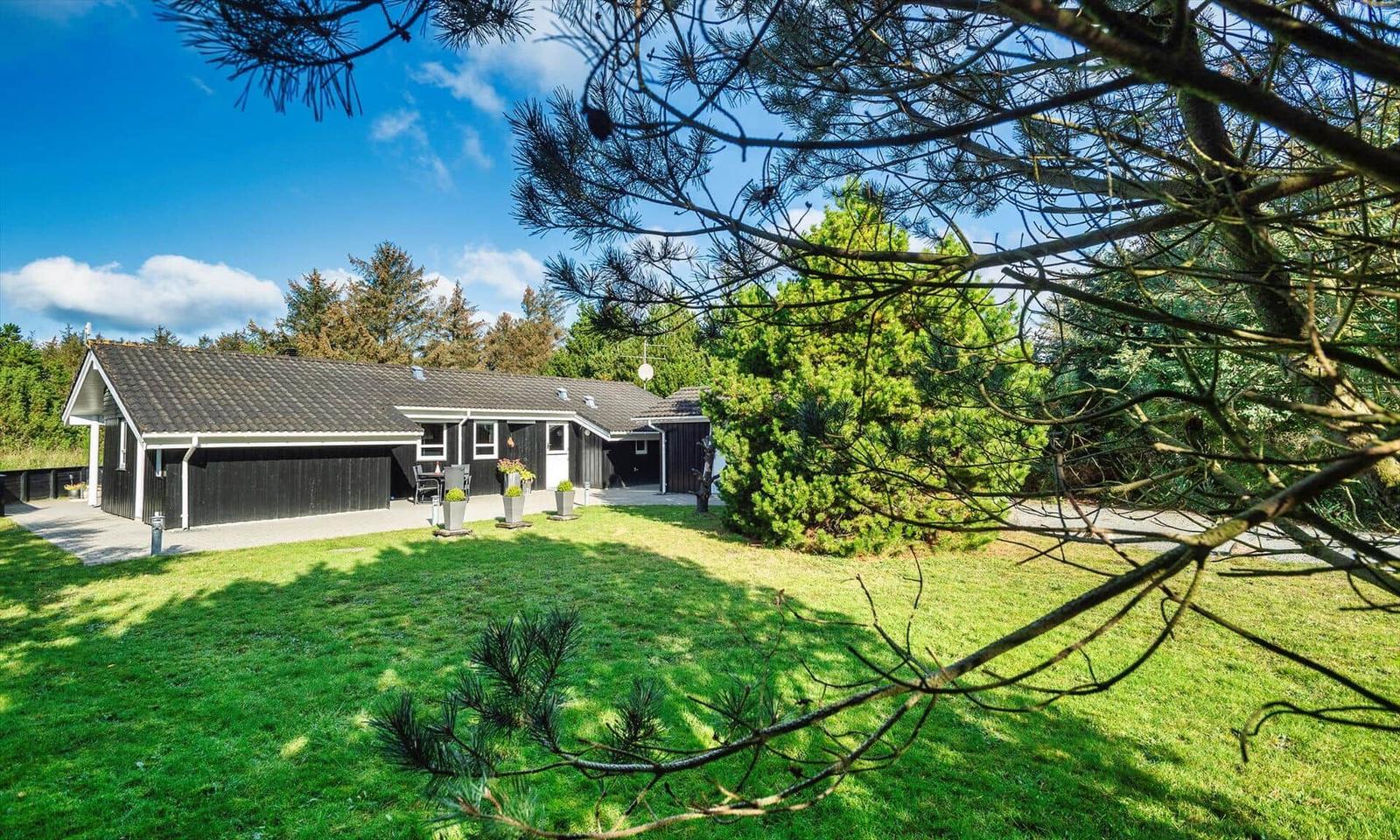 Schwarzes Haus mit Garten und Bäumen unter blauem Himmel.