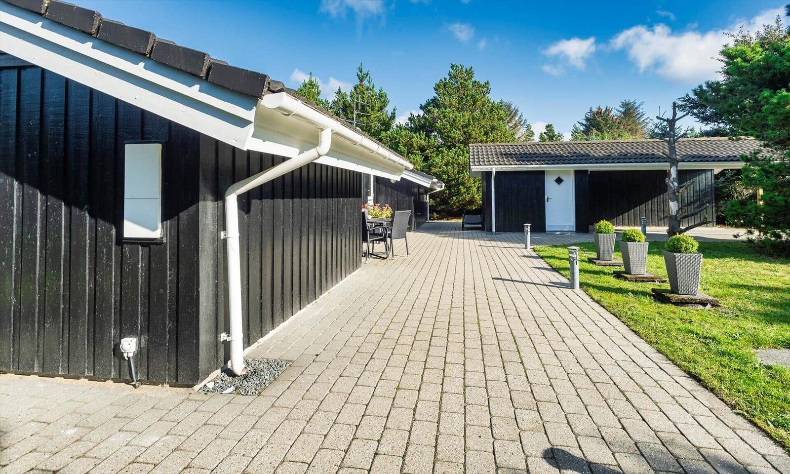 Pflasterweg führt zu einem Haus mit dunkler Holzfassade und Garten.
