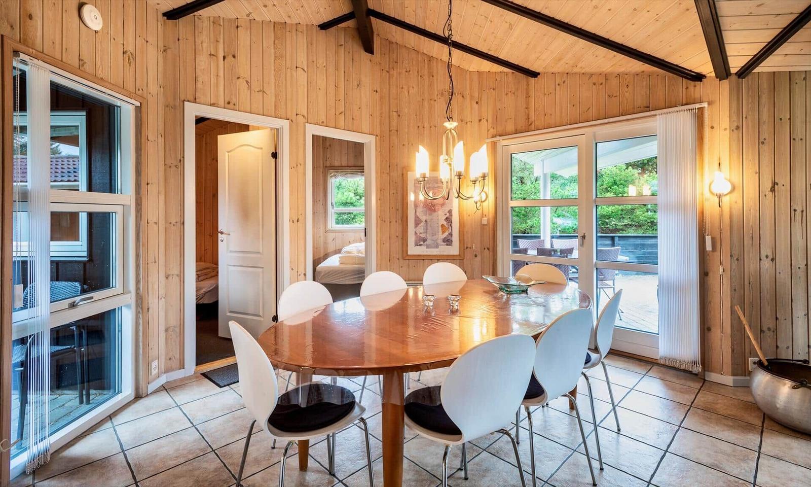 Esszimmer mit Holzwand und runden Tisch. Durchgänge zu Schlafzimmern. Fenster zur Terrasse.