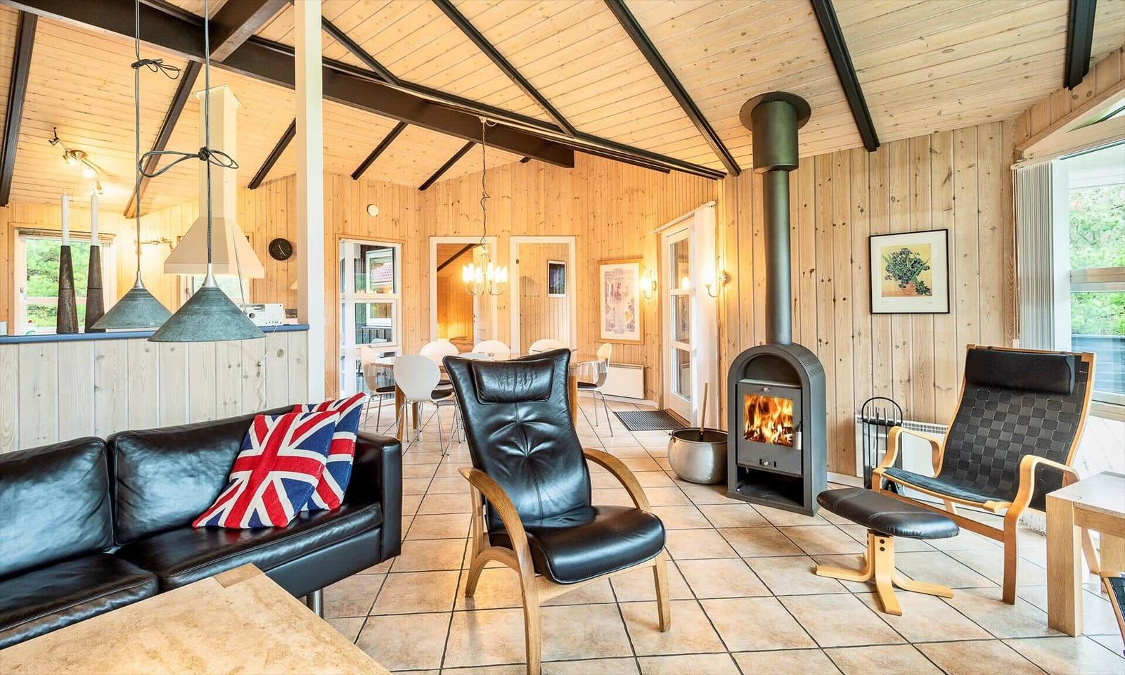 Wohnraum mit Kamin, Ledersofa und Holzwänden. Blick in Essbereich und Schlafzimmer.