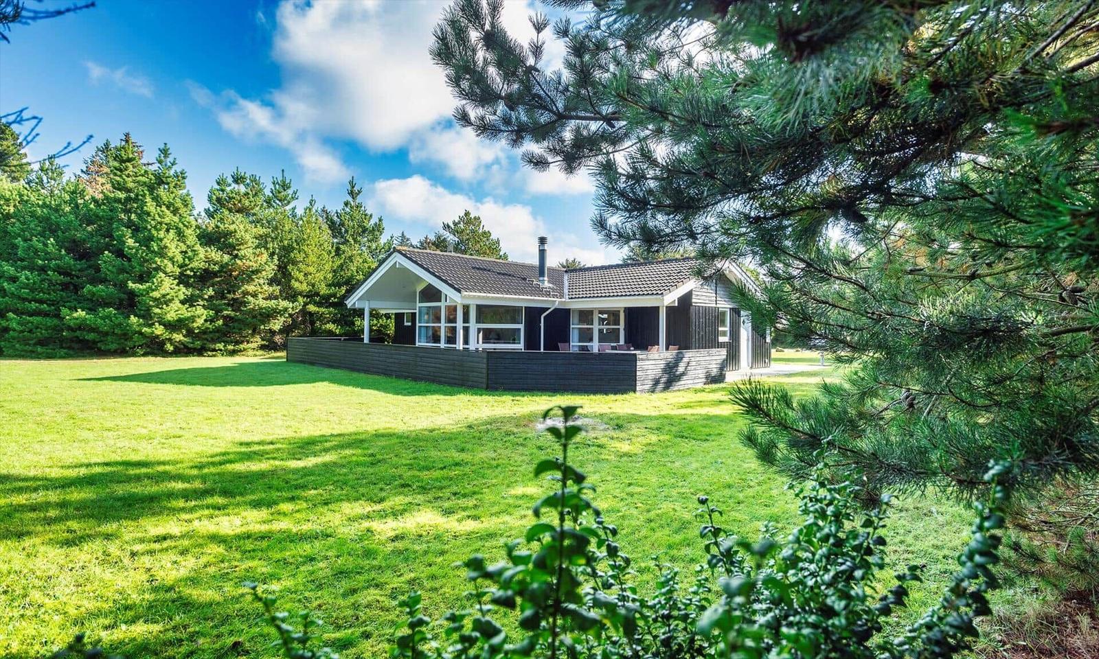 Ein modernes Haus mit Terrasse steht auf einer grünen Wiese zwischen Bäumen.