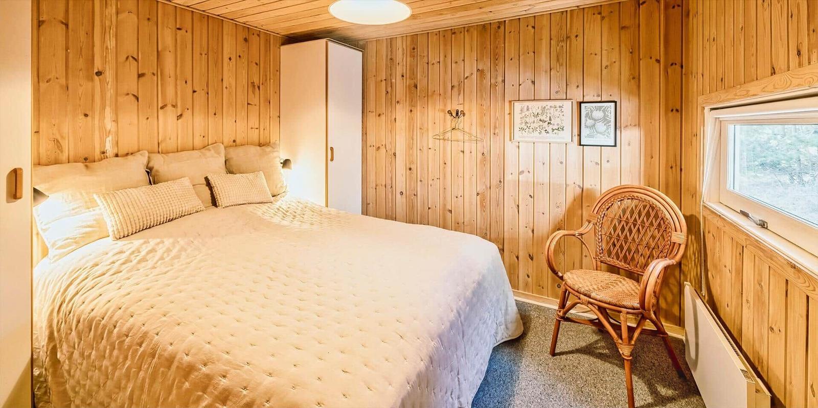 Schlafzimmer mit Holzwand, Bett, Stuhl und Fenster