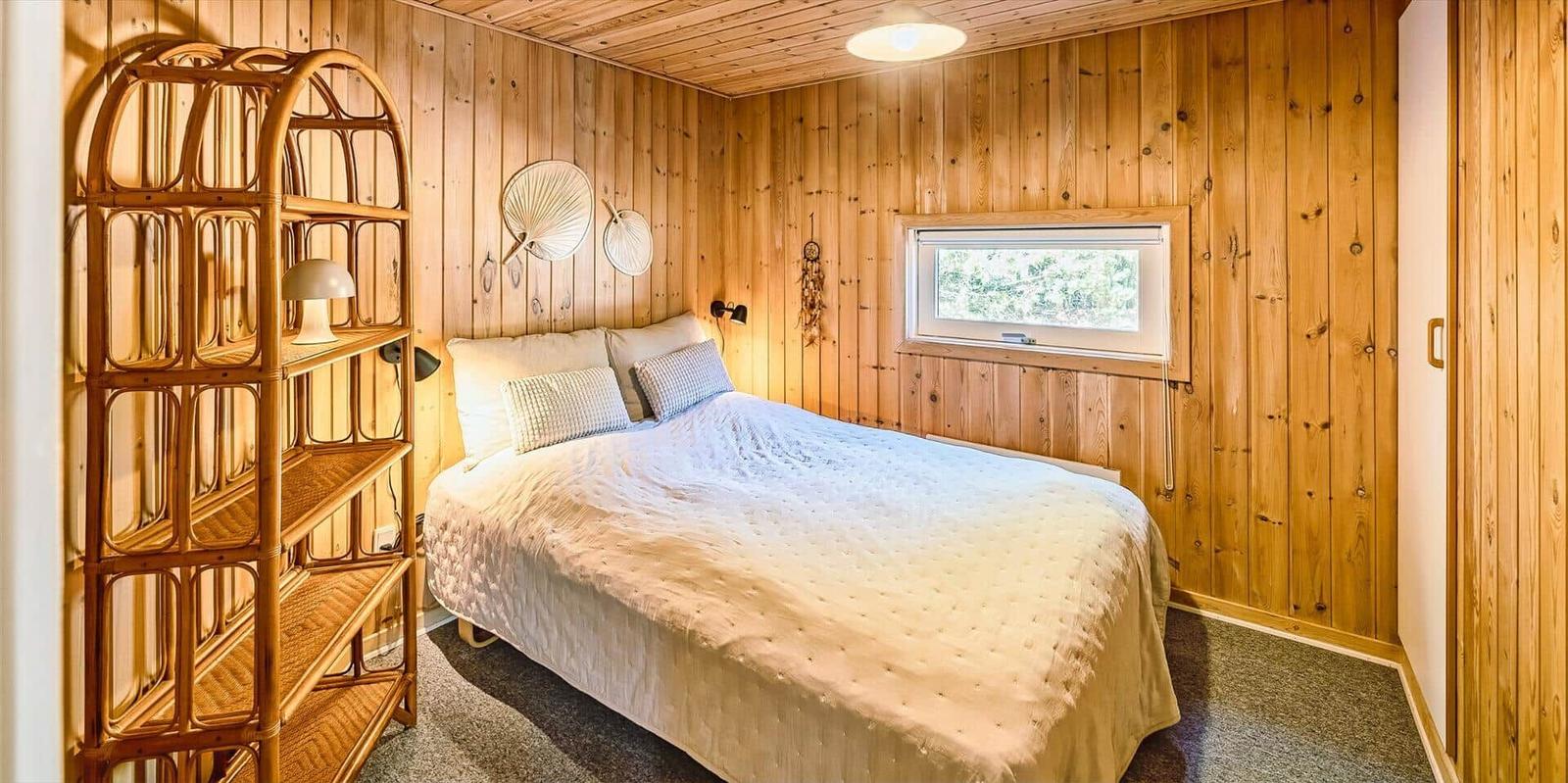 Schlafzimmer mit Holzwand, Bett und Fenster. Holzregal links. Wanddekoration.