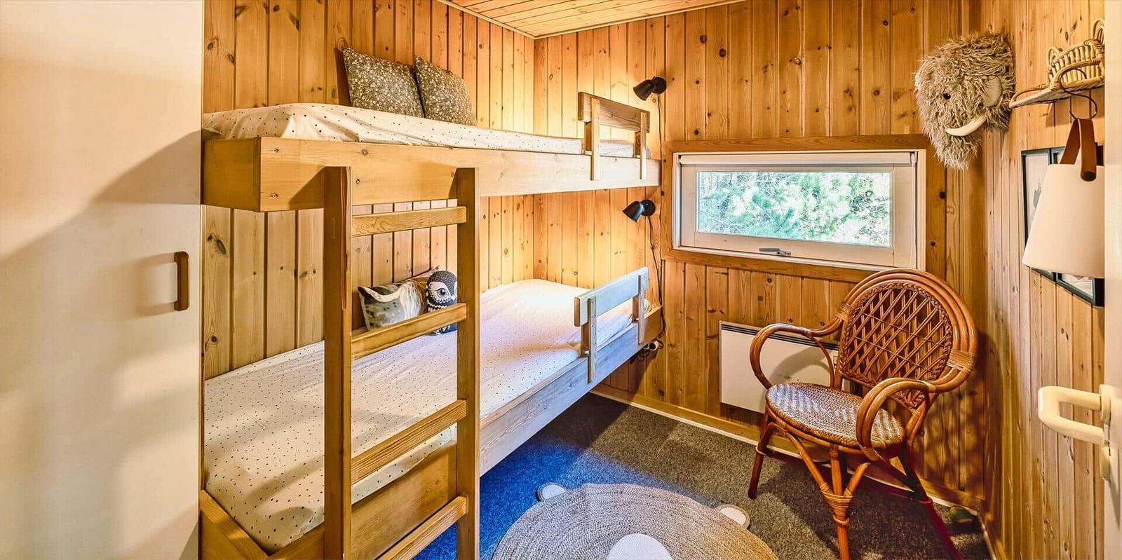 Kinderzimmer mit Doppelstockbett, Stuhl und Fenster zum Wald.
