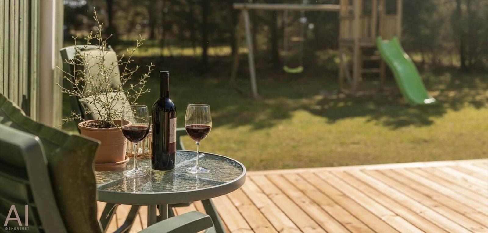 Auf der Terrasse steht ein Tisch mit Wein und einer Pflanze. Im Hintergrund ist ein Spielplatz mit Rutsche.