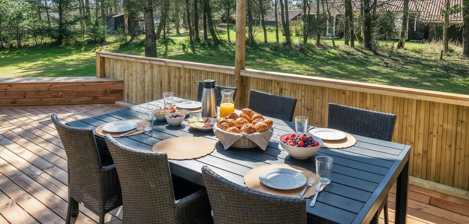 Terrasse mit Esstisch, Stühlen und Frühstückszubehör im Freien.