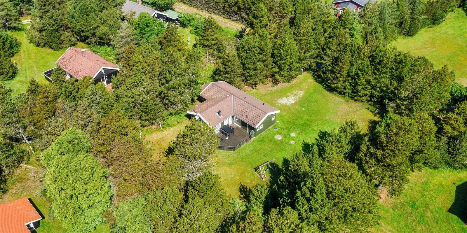 Haus mit Terrasse und Garten, umgeben von Bäumen und Grasflächen.