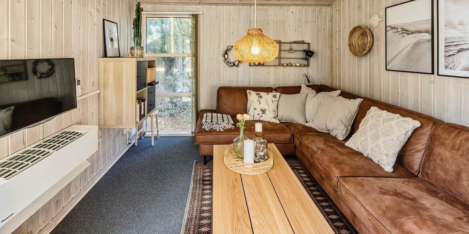 Wohnzimmer mit braunem Sofa, Holztisch und Fernseher an der Wand.