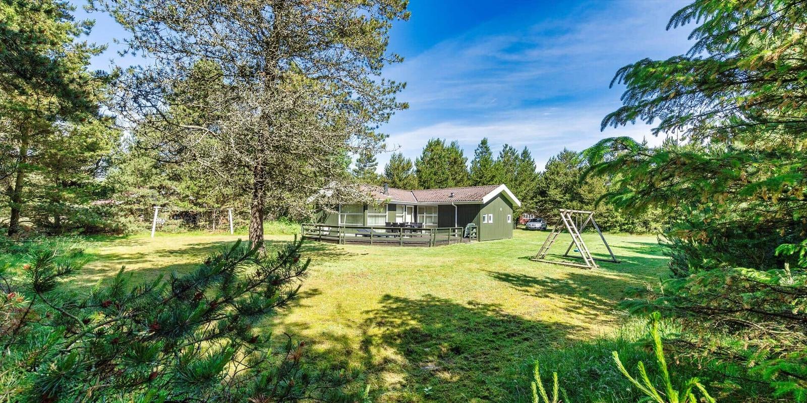Grünes Ferienhaus mit Terrasse, Spielplatz und umgeben von Bäumen.