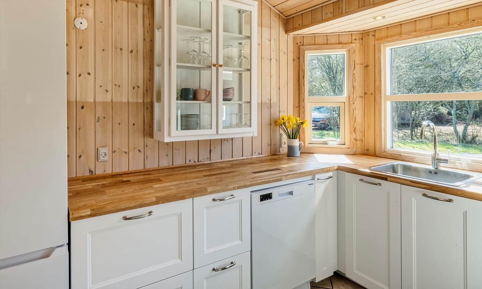 Küche mit Holzwand, weißen Schränken und Fenster zum Garten.