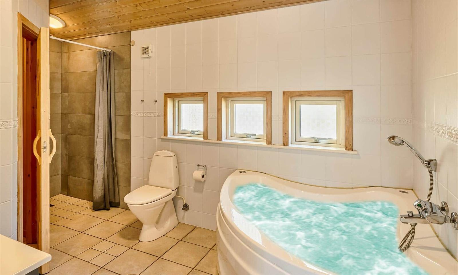 Bad mit Whirlpool, Toilette und Dusche mit Holzdecke und Fenstern.