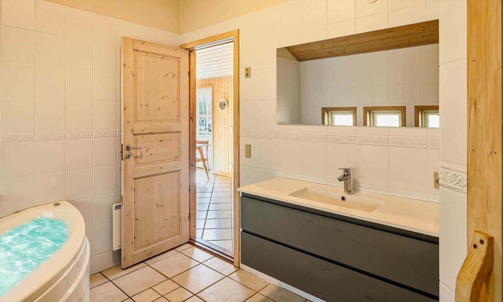 Badezimmer mit Whirlpool, Waschbecken und Spiegel. Holztür führt nach draußen.