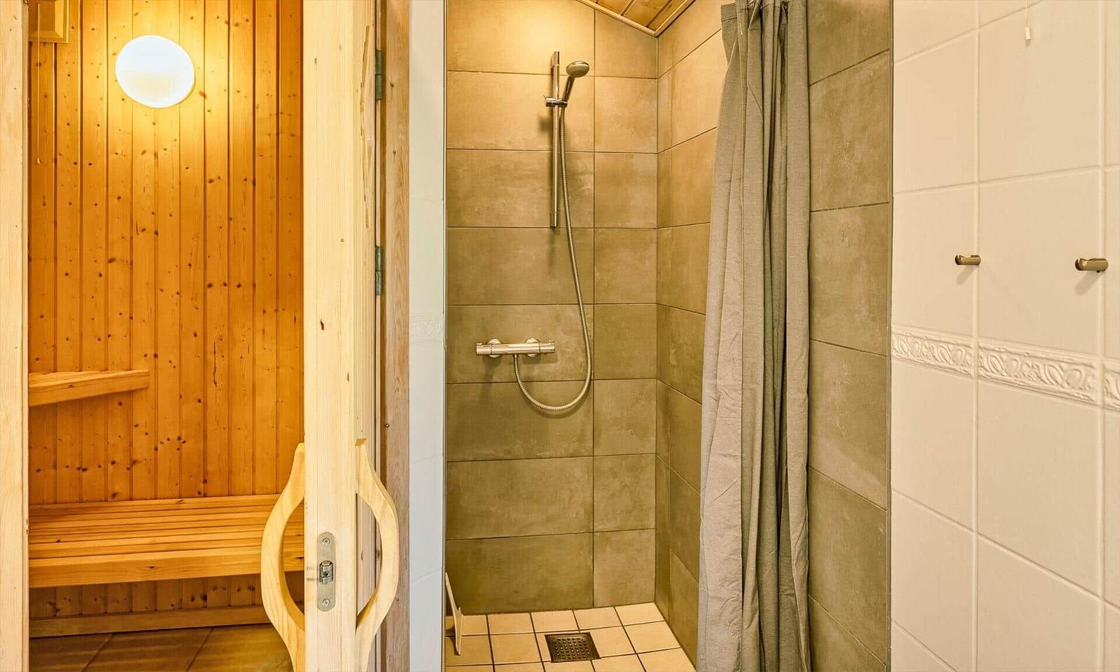 Dusche mit Duschbrause und Duschvorhang neben Sauna mit Holzbank.