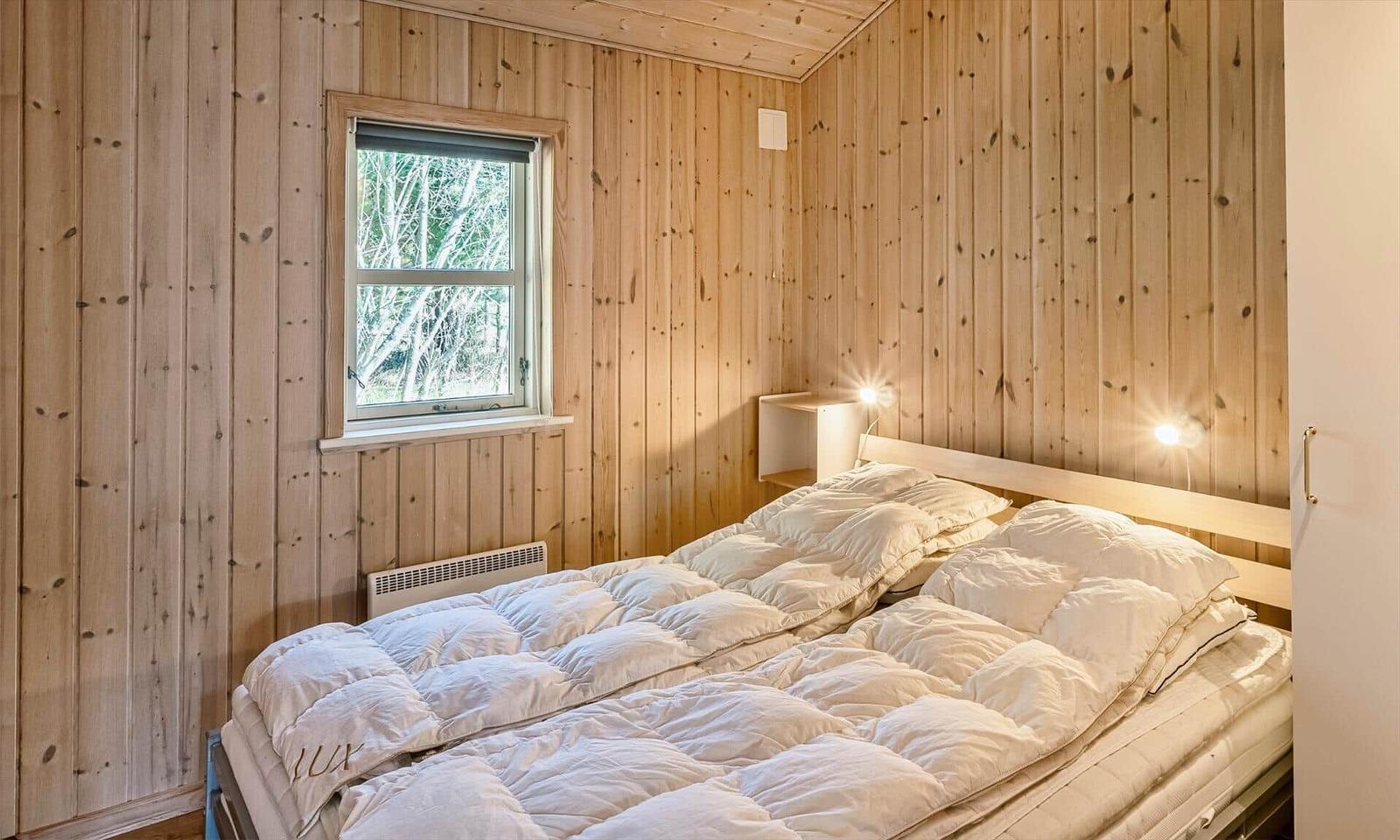 Schlafzimmer mit Holzwänden, Bett und Fenster.