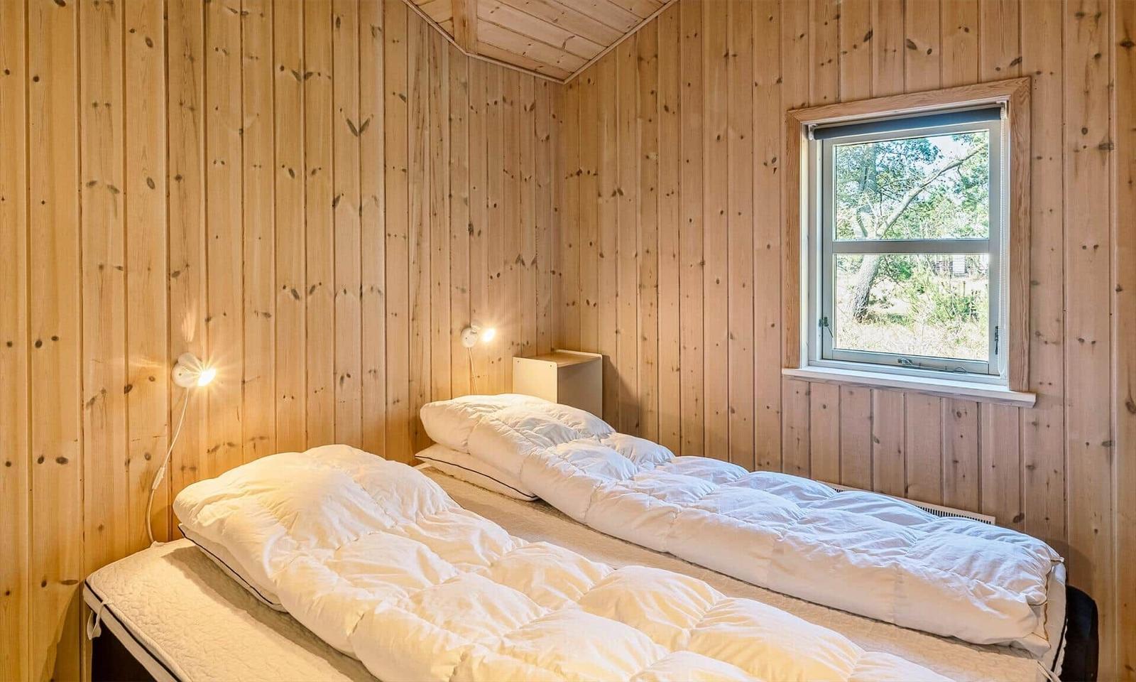 Zwei Betten in einem holzverkleideten Raum mit Fenster und Nachttisch.