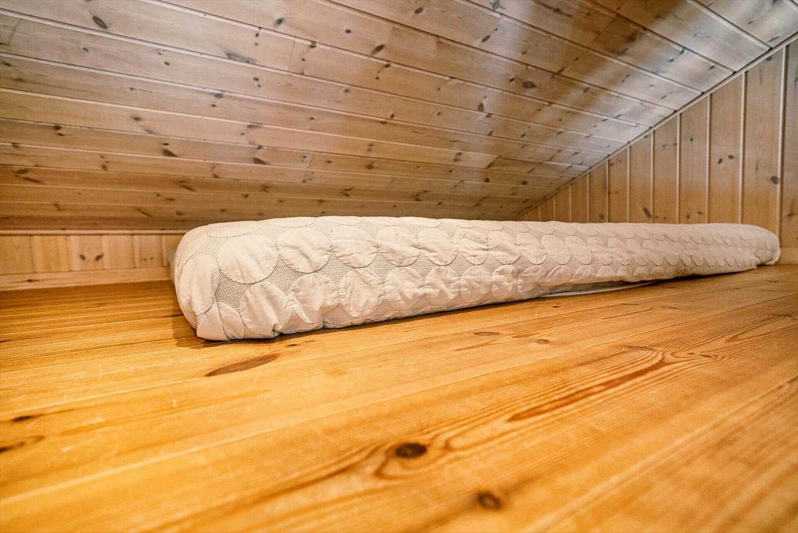 Ein Bett mit Muster liegt auf Holzboden in einem holzverkleideten Raum.