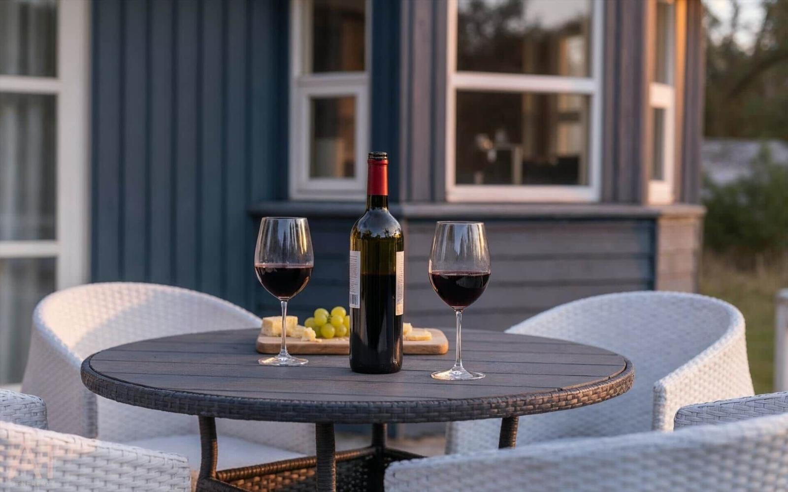 Runder Tisch mit Wein, Käse und Trauben auf Terrasse vor Haus.