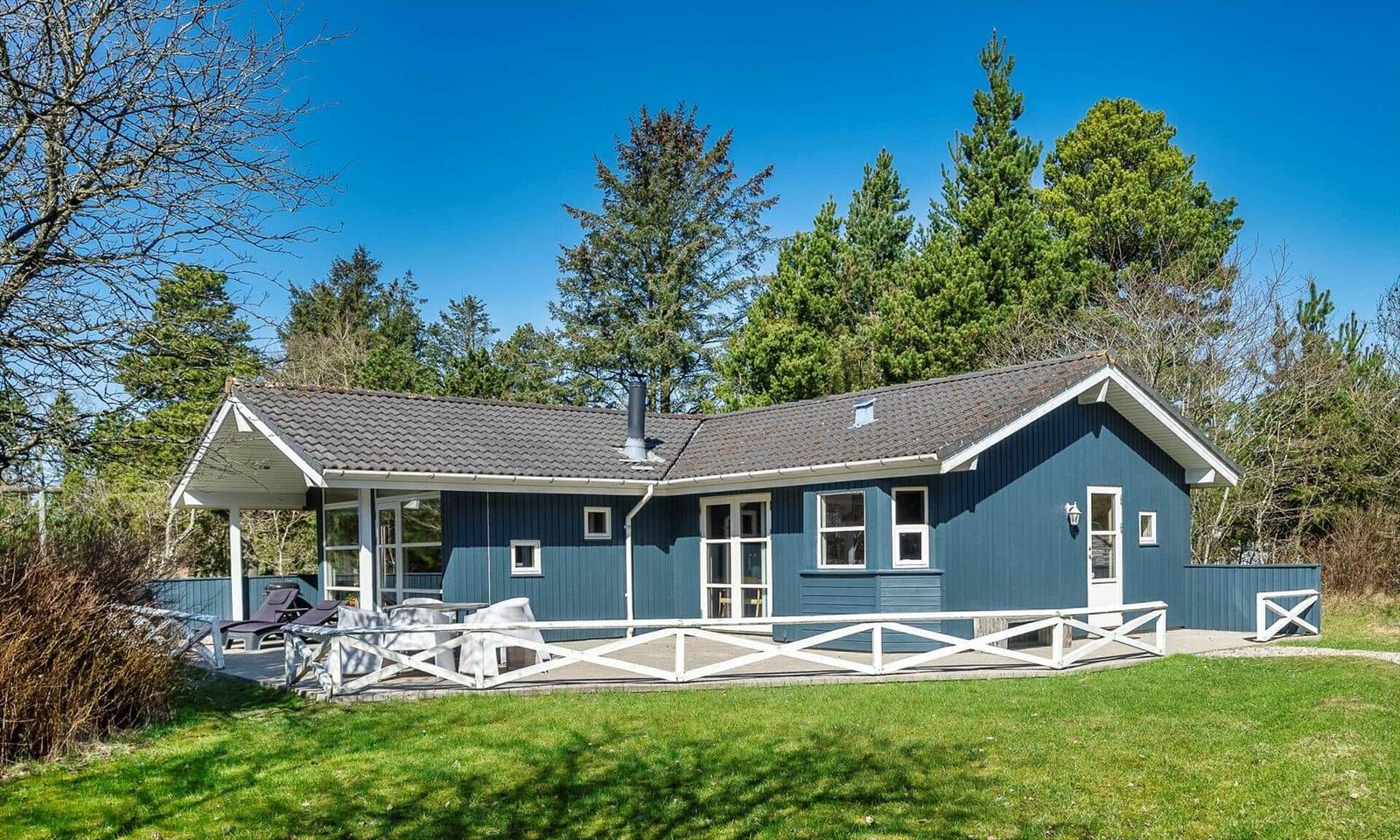 Ein blaues Ferienhaus mit weißem Geländer und Terrasse unter Bäumen.